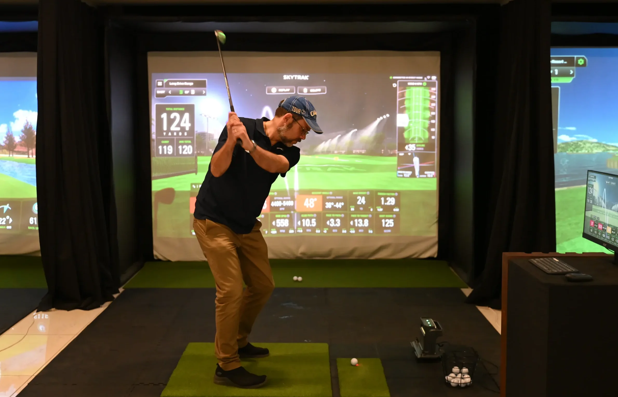 Man taking a full golf swing inside an indoor golf simulator at an indoor golf facility.
